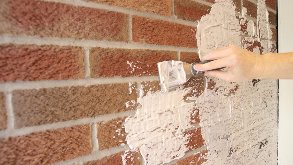 woman spreading joint compound on brick textured wall